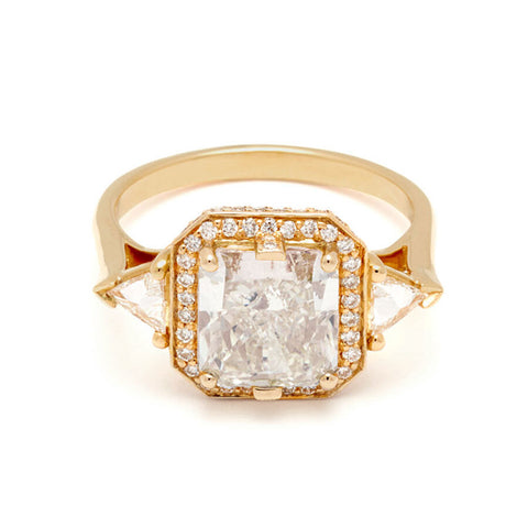 A radiant cut lab white diamond encircled by a white diamond halo and two white lab trillion diamond side stones set in a yellow gold ring on a white background 
