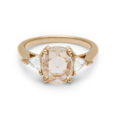 A three stone engagement ring with a cushion cut champagne diamond center stone with two white diamond trillion side stones set in yellow gold.