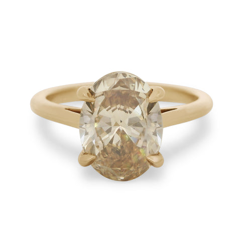 A champagne oval diamond engagement ring set in yellow gold on a white background