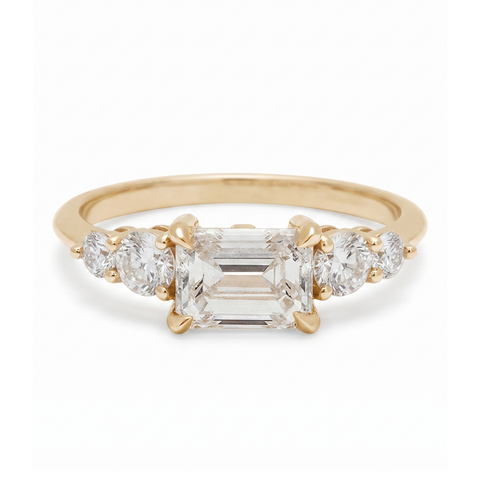 Gold ring with a central emerald-cut diamond and two side stones on a white background