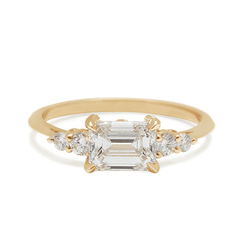 Gold ring with emerald-cut diamond and smaller diamonds on a white background