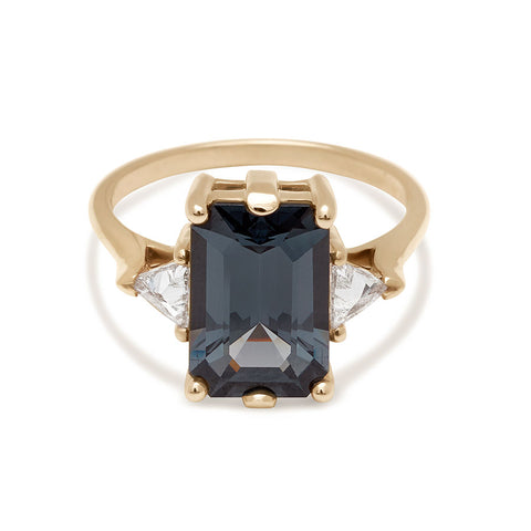 Gold ring with a dark grey spinel gemstone and smaller white triangle diamond side stones on a white background 5