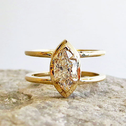 A double banded bezel set marquise champagne diamond ring set in yellow gold on a grey rock.