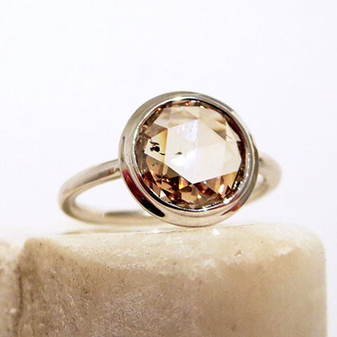 A round rose cut bezel set champagne diamond set in white gold on a white stone.