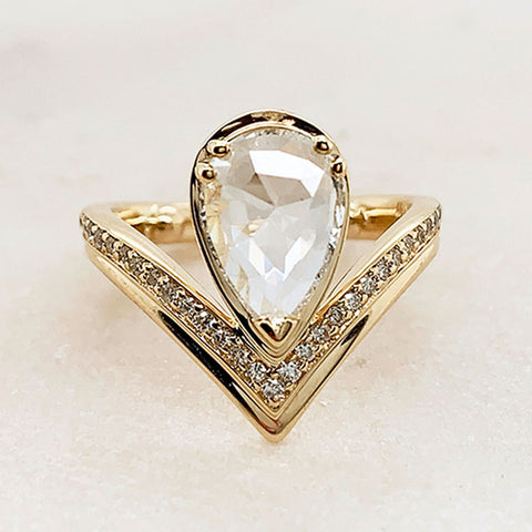 A pear shaped rainbow moonstone set above a white diamond dusted band set in yellow gold on a grey background.