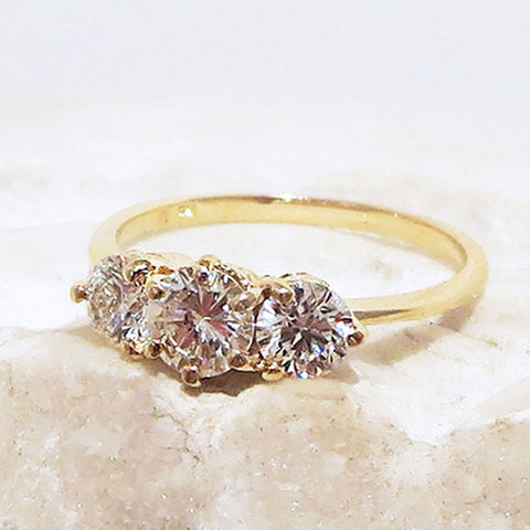 A three stone engagement ring with a round shape champagne diamond center stone with two white diamond round side stones set in yellow gold on a white stone.