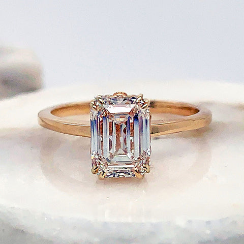 A solitaire emerald cut white diamond ring with double claw prongs set in yellow gold on a stone.