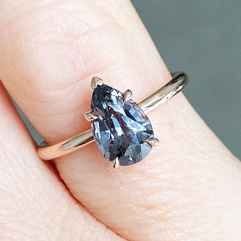 A solitaire pear grey spinel ring with claw prongs set in white gold on a light-complextion model's hand.