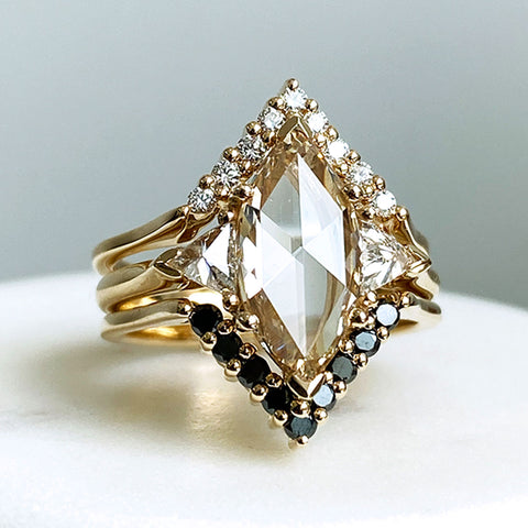 A three stone engagement ring with a marquise shape champagne diamond center stone with two white diamond trillion side stones set in yellow gold stacked in between two diamond nesting bands.