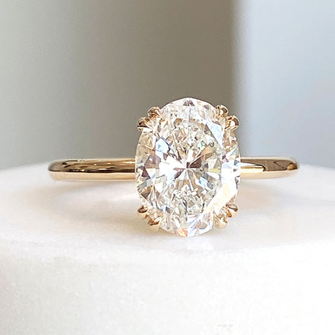 A solitaire oval white diamond ring with double claw prongs set in yellow gold on a white stone.