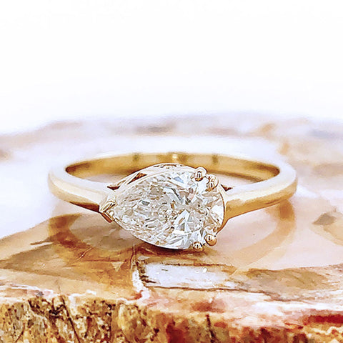 A pear shaped ring with a white diamond stone set in yellow gold and placed on a piece of wood.
