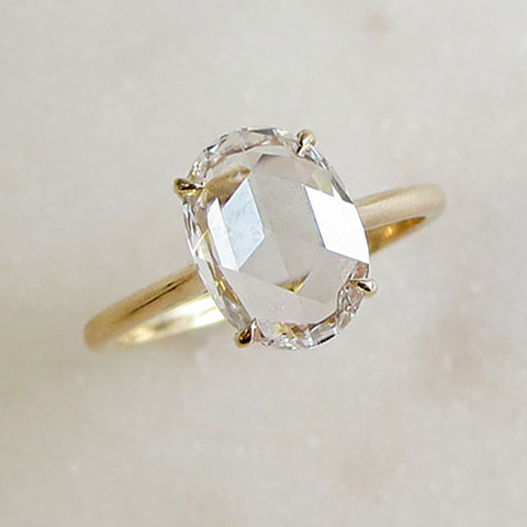 A solitaire ring rose cut oval white diamond set in yellow gold on a grey background.