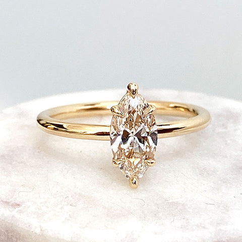 A solitaire marquise champagne diamond ring with claw prongs set in yellow gold on a grey stone.