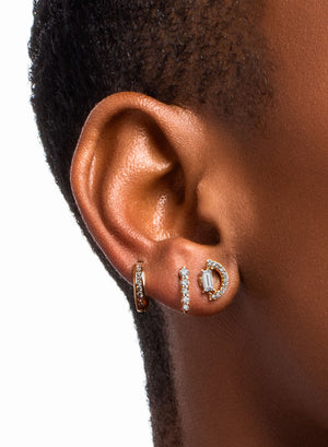 A model with a darker complexion wears three diamond earrings. An arc diamond stud, a pave stud, and a hoop with pave diamonds.