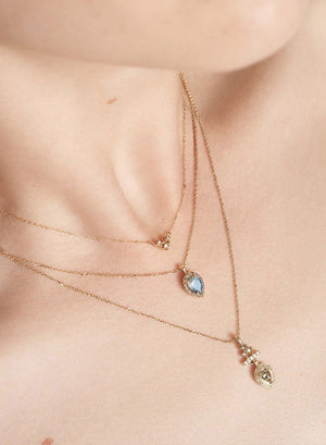 A lighter-complexion model's chest that holds three chain necklaces. One with 3 champagne diamonds, one with a pear shaped gemstone, and one featuring pearls and two shades of diamonds.