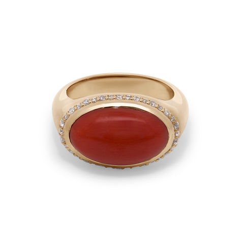 A yellow gold ring featuring a red coral cabochon center and a champagne diamond halo on a white background