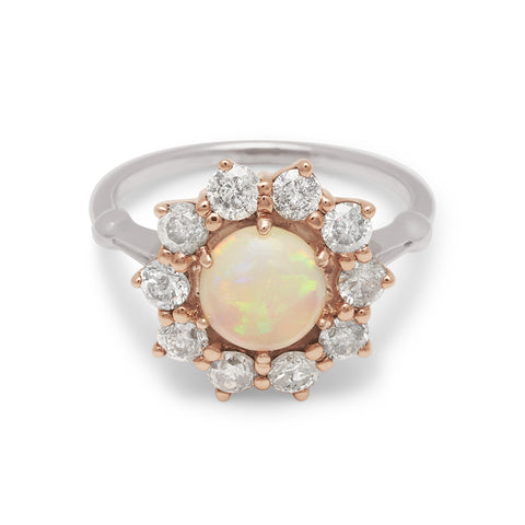 A ring with a round opal center stone surrounded by round grey diamonds set in a rose gold basket and a white gold band.