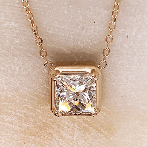 A square princess cut white diamond bezel set in yellow gold on a yellow gold chain.