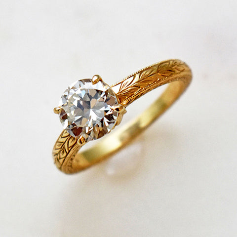 A solitaire ring round white diamond set in yellow gold with a wheat engraving on the band.