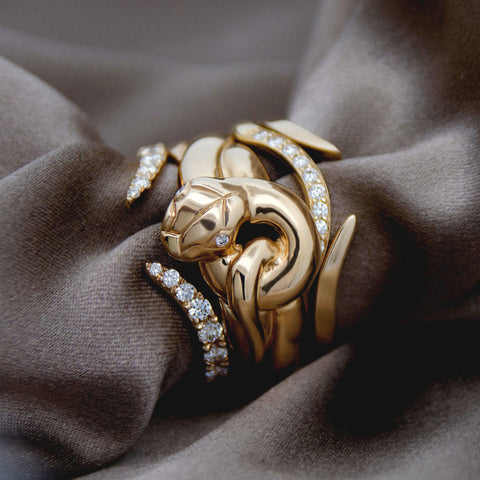 Gold serpent-shaped ring with diamond accents and other diamond and gold nesting bands on brown fabric 4