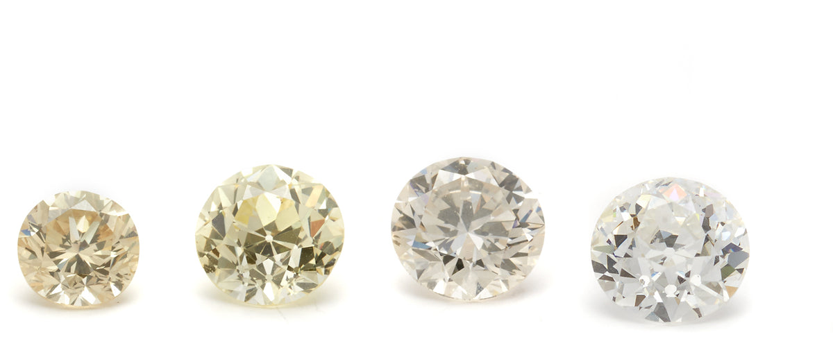 4 round cut diamonds sit horizontally across the image, graduating in color from yellow diamond to white diamond