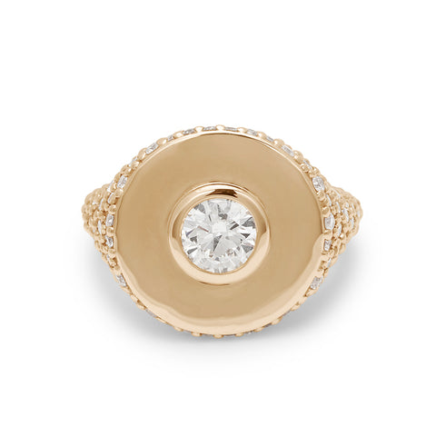 Front view of a round white diamond bezel set in a signet style ring with white diamond pave down the sides of the band set in yellow gold.