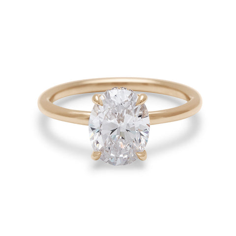 An oval shaped lab white diamond solitaire engagement ring with a hidden white diamond pave halo under the center stone set in yellow gold.