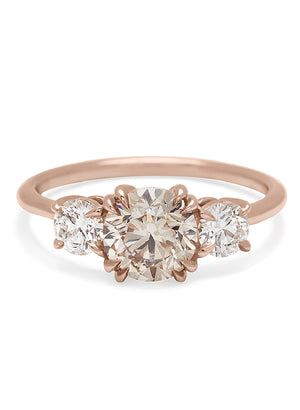 A three stone engagement ring with a round shape champagne diamond center stone with two white diamond round side stones set in rose gold.