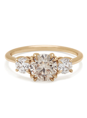 A three stone engagement ring with a round shape champagne diamond center stone with two white diamond round side stones set in yellow gold.