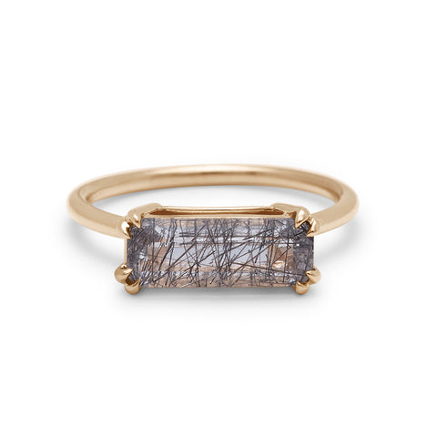 An elongated east/west solitaire ring with an elongated emerald shape black rutilated quartz stone set in yellow gold.