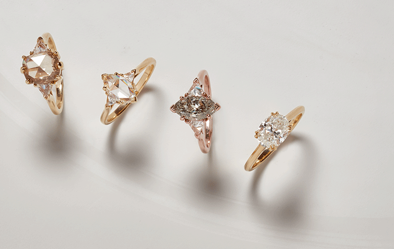 An array of 4 gold engagement rings. Two feature champagne diamond center stones and two feature white diamond center stones on a light-grey background.