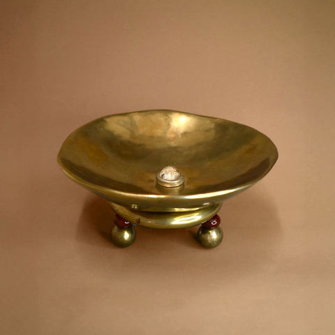 Brass bowl with a quartz in the middle and red carnelian and bronze feet on a beige background