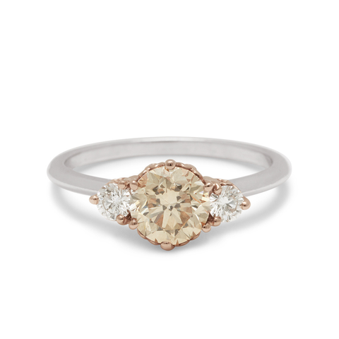 A three stone engagement ring with a round shape champagne diamond center stone with two white diamond round side stones set in a rose gold basket and a white gold band.