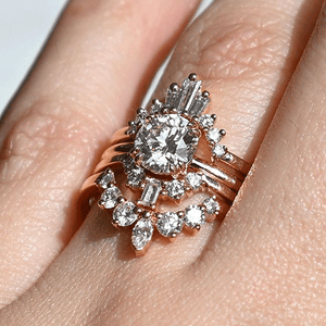 A close up of a ceremonial stack featuring an engagement ring with various white diamond curved wedding bands with diamond baguettes and diamond marquise stones.