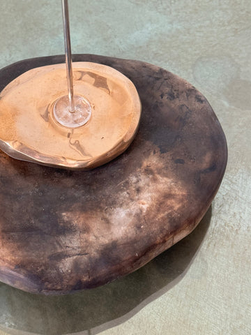 Large pit-fired stone object with a bronze dish adhered to the top with clear-white flower quartz on a glass table