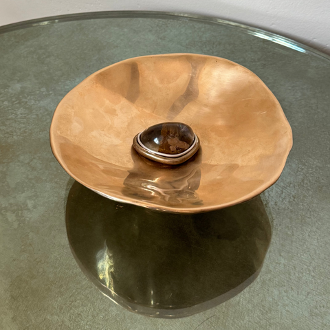 Bronze bowl with brown quartz on a glass table with a plain background