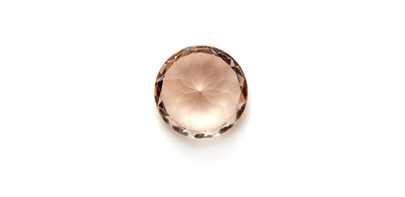 A round brilliant morganite on a flat surface and white background