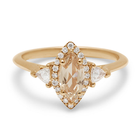 A three stone engagement ring with a marquise shape rose cut 0.60ct champagne diamond center stone surrounded by a white diamond pave halo with two white diamond trillion side stones set in yellow gold.