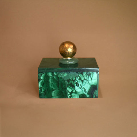 Malachite box with an Aventurine gemstone and bronze ball on top of lid on a beige background