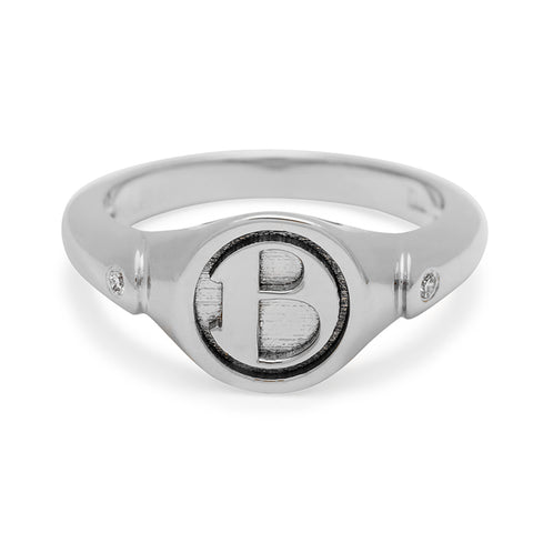 A monogrammed signet ring with a "B" on the front and two grey diamond accents on either side and set in sterling silver.
