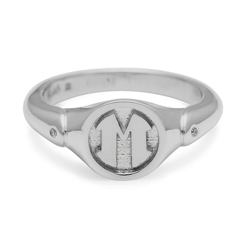 A monogrammed signet ring with a "M" on the front and two grey diamond accents on either side and set in sterling silver.