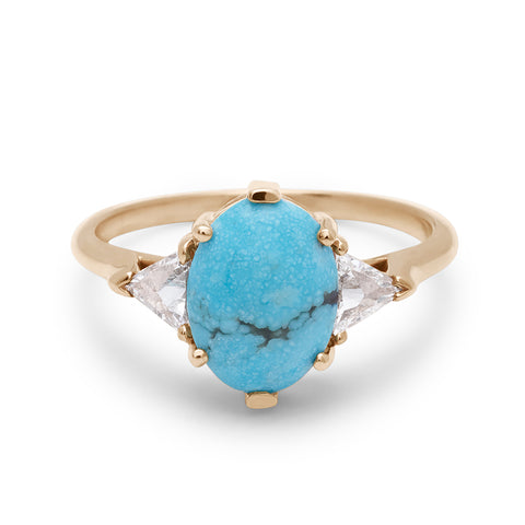 A three stone engagement ring with an opal shape turquoise center stone with two white diamond trillion side stones set in yellow gold.