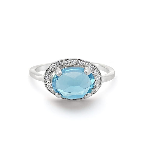 A ring with an oval shape blue topaz center stone surrounded by a champagne diamond pave halo set in sterling silver.