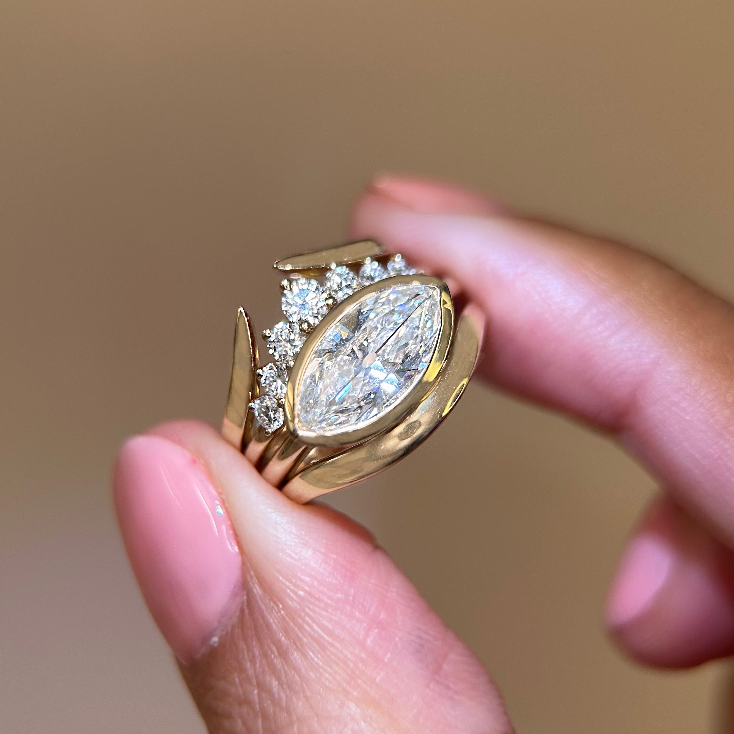 Gold ring with a large diamond held between two fingers against a neutral background