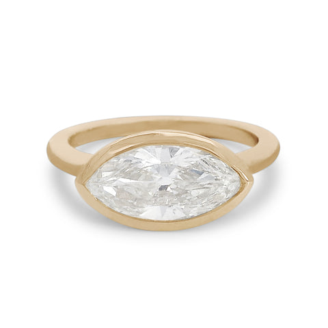 A white moval cut diamond set east west in a yellow gold bezel setting. 