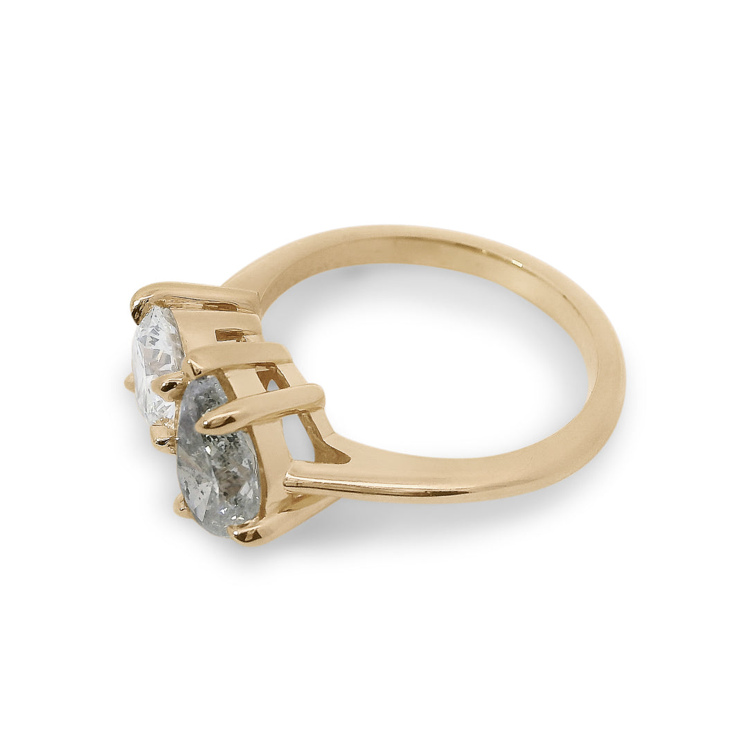 Two diamond toi et moi ring featuring a round brilliant white diamond and a pear shaped grey diamond with gold setting on a white background