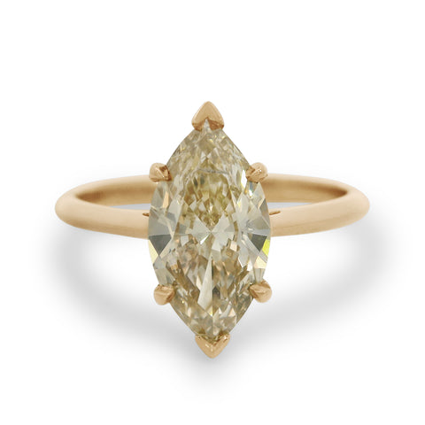 A champagne marquise cut diamond solitaire ring set in yellow gold on a white background