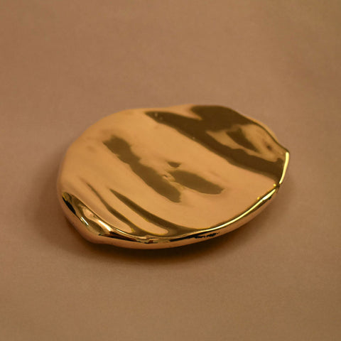 Flat, rippled, footed bronze dish on a beige background