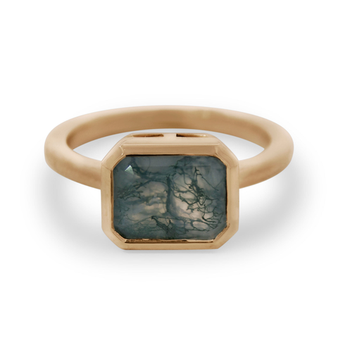 A yellow gold bezel ring featuring an emerald cut green moss agate gemstone on a white background