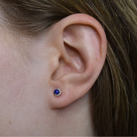 Close-up of an ear wearing a blue lapis lazuli gemstone earring which features a champagne diamond halo and is set in sterling silver. 2